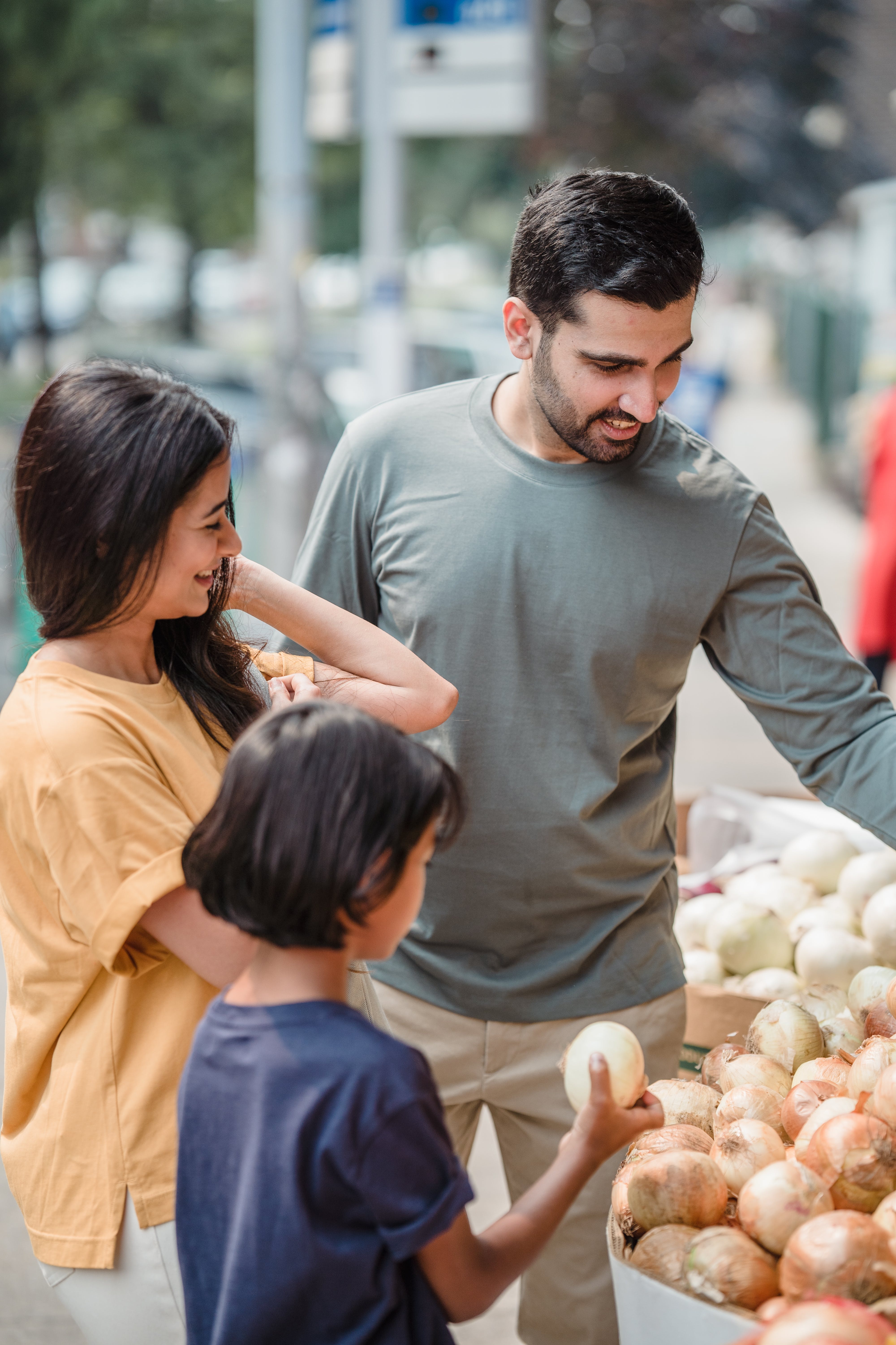 A man, a woman, and a child picking up onions at the farmer's market.