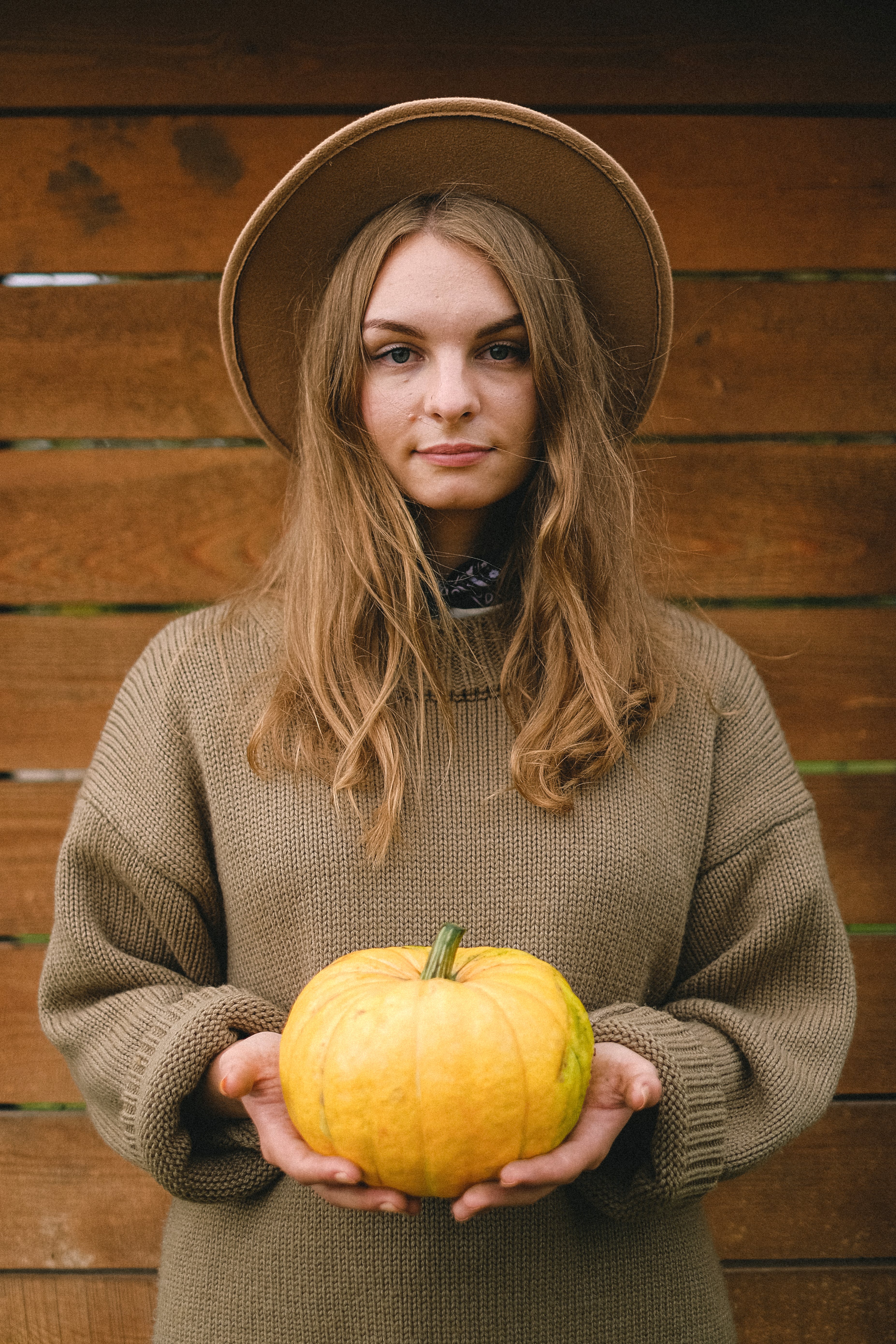 A woman wearing a sun hat, and holding her prized yellow pumpkin.