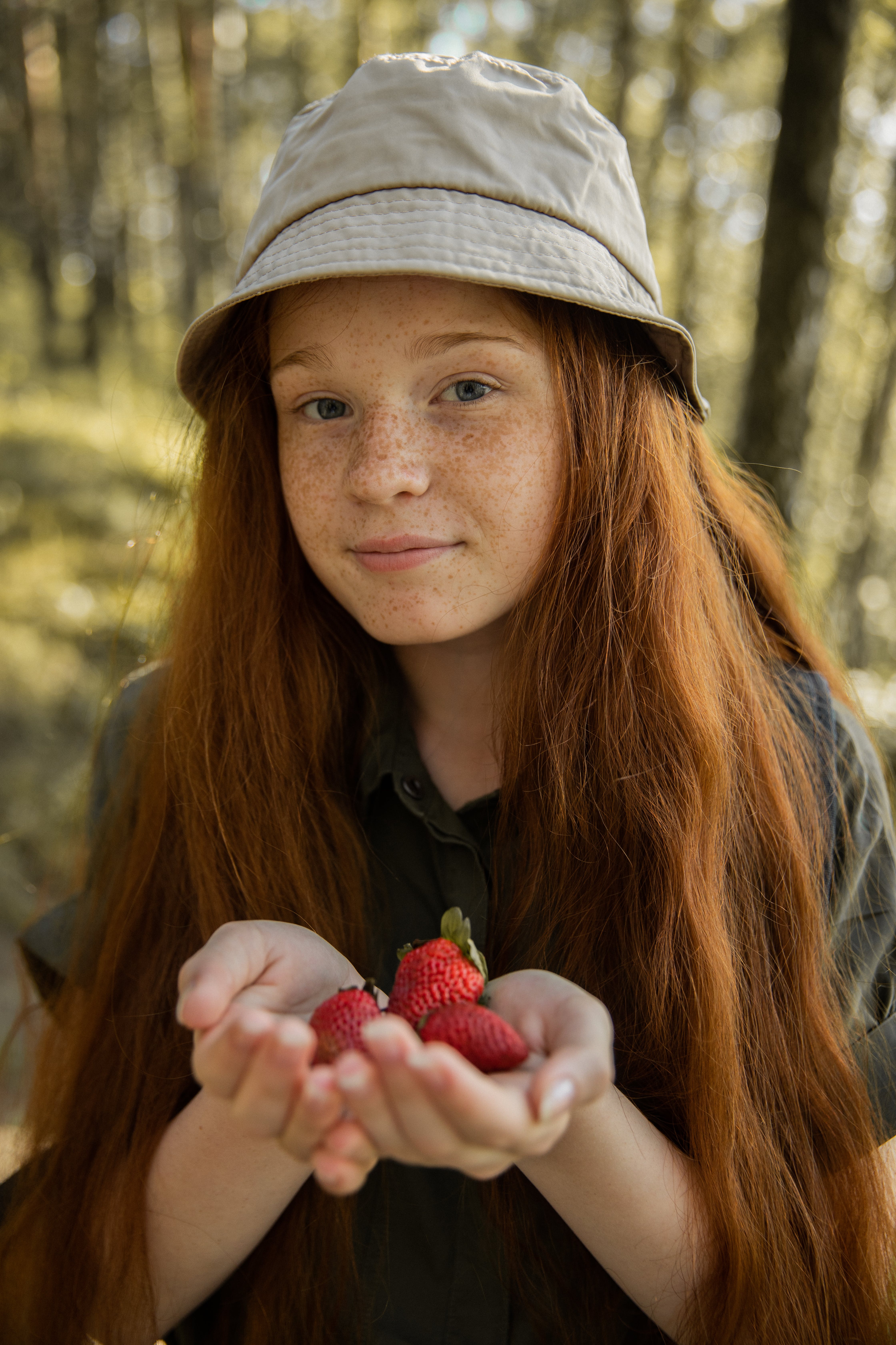 A woman wearing a bucket hat, holding her homegrown strawberries.